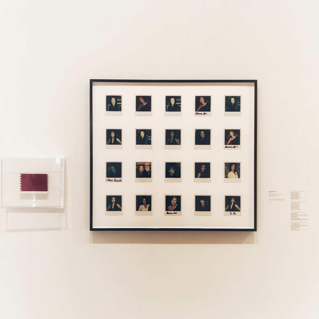 A framed grid of twenty polaroid portraits on a white wall